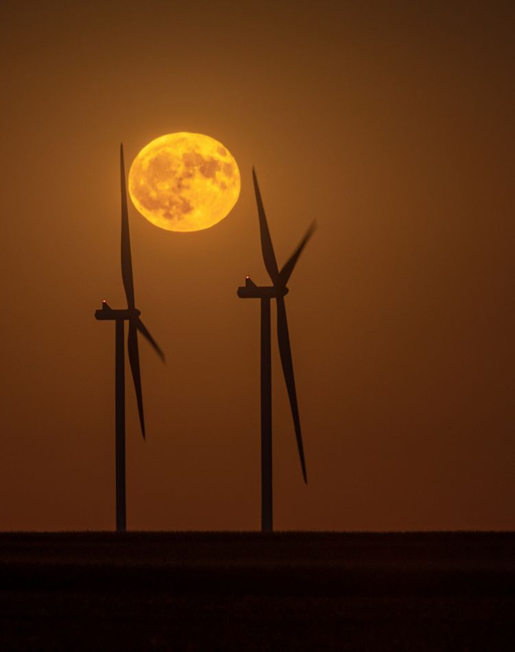 The full moon rises above windmills.
