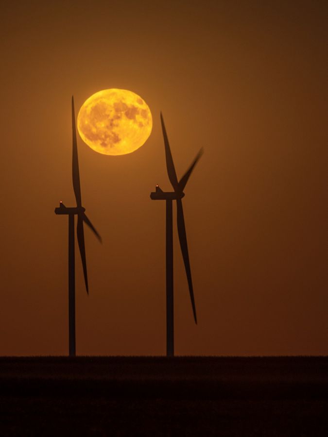 The full moon rises above windmills. 
