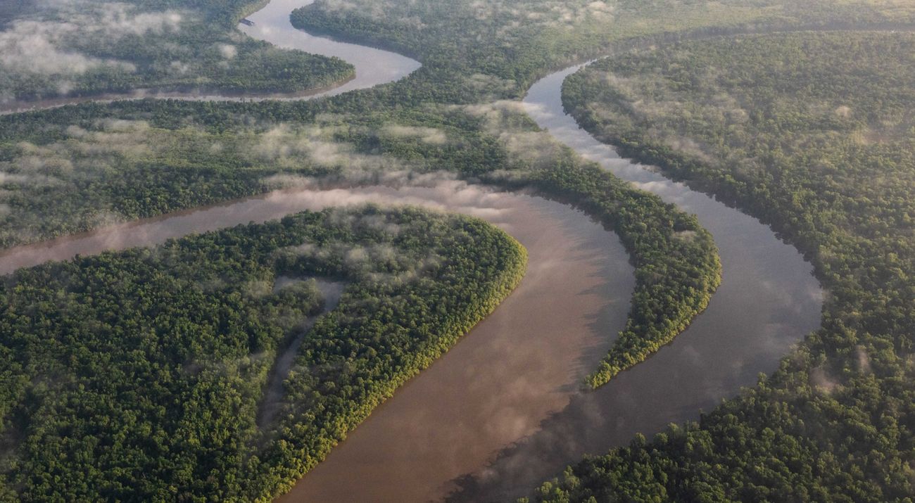 Wispy clouds float over a winding river seen from above.