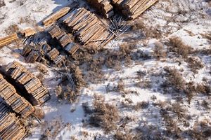Aerial view looking down at piles and bundles of wood planks in a snowy landscape.