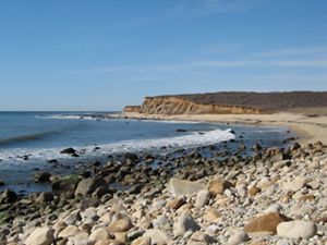 Waves lapping against a beach with cliffs in the background.