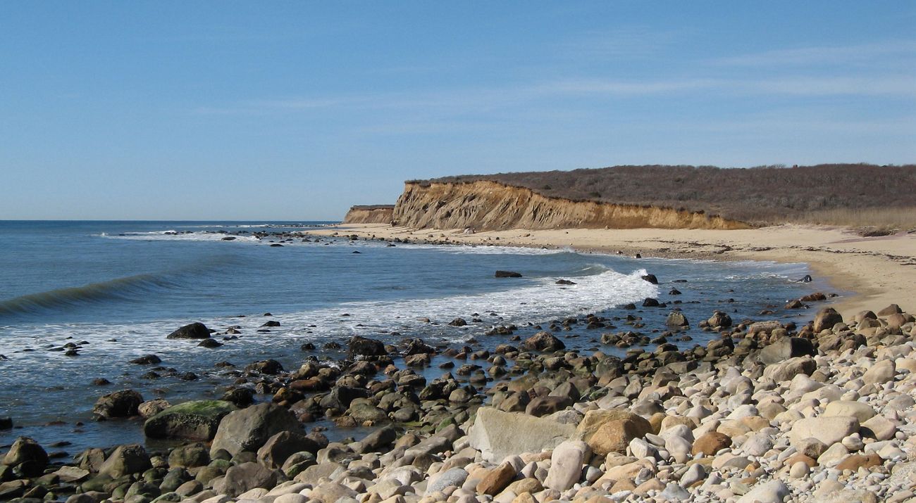 Waves lapping against a beach with cliffs in the background.