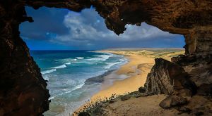 View from inside a cave of ocean waves meeting beach and shoreline.