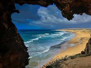 View of ocean waves meeting beach and coastline from inside a cave.