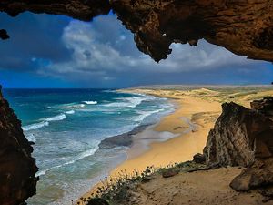View from inside a cave of ocean waves meeting beach and coastline.