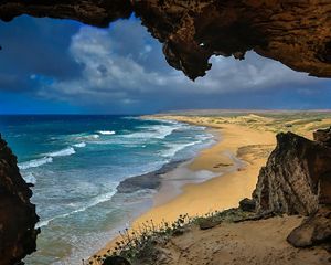View from inside a cave of ocean waves meeting beach and coastline.