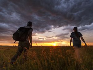 Two hikers walking in a prairie toward the setting sun.