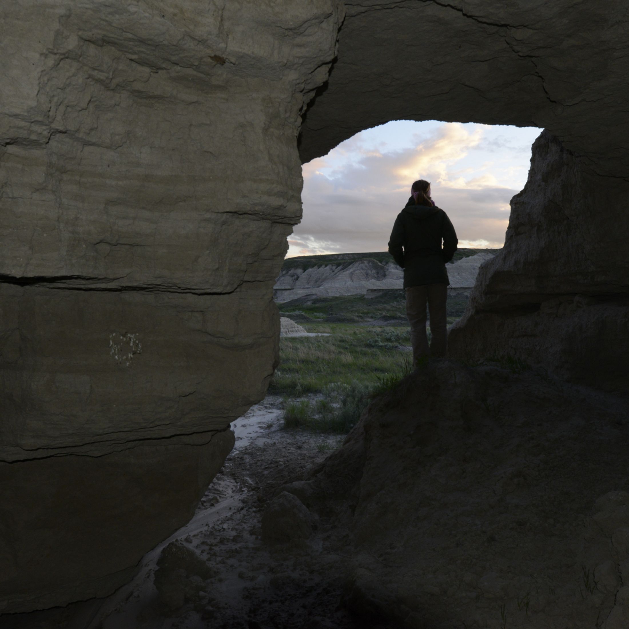 A person stands in a rocky outcrop and looks out over the Conata Basin prairie.