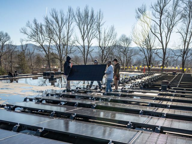 People working together to move a solar panel amongst a solar installation on a roof.