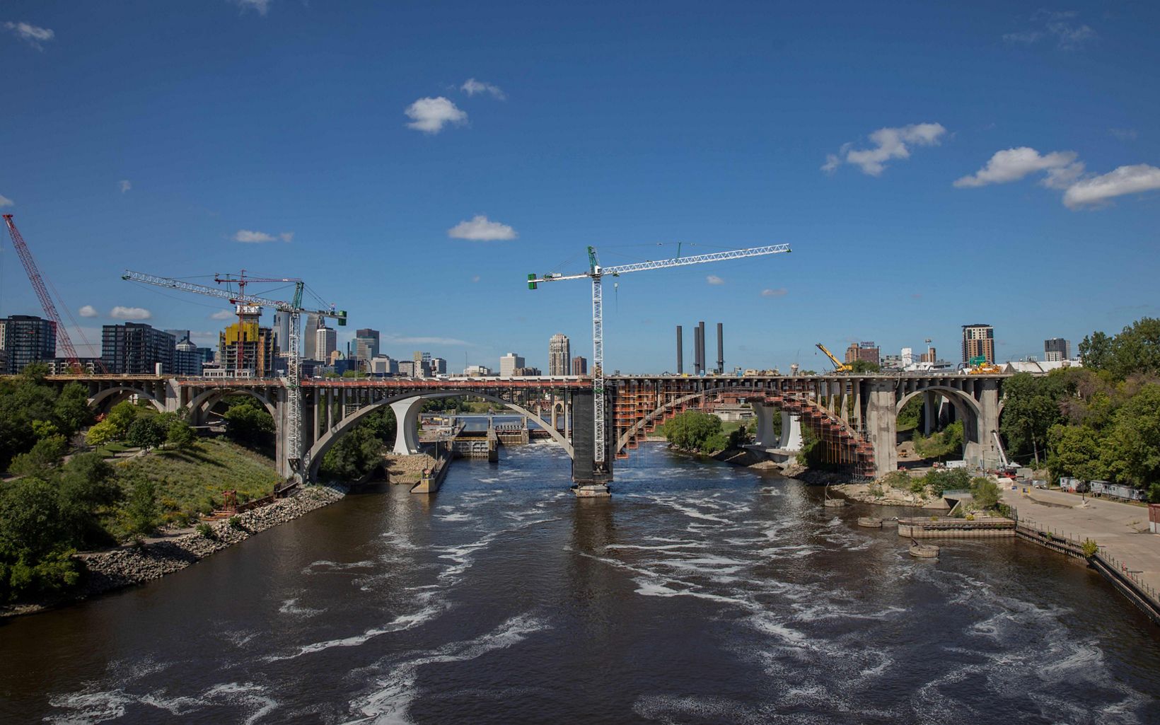 A view of a bridge under construction over the Mississippi River, with downtown Minneapolis in the background.