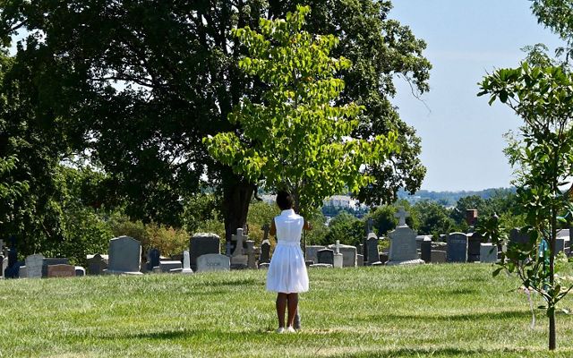 Tying a prayer ribbon to a tree at Mount Olivet Cemetery during a celebration of the legacy of freedmen John and Arabella Weems. 