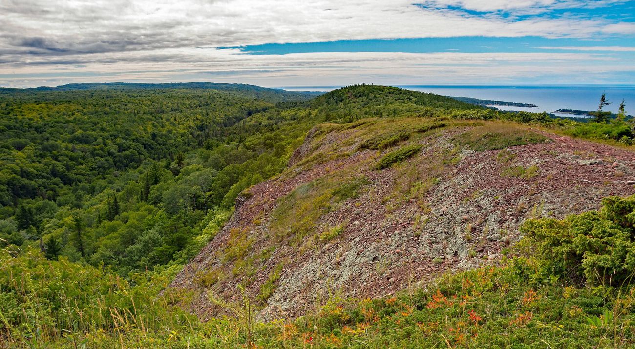A bald, rocky hilltop with views of forested hills and a lake in the distance.