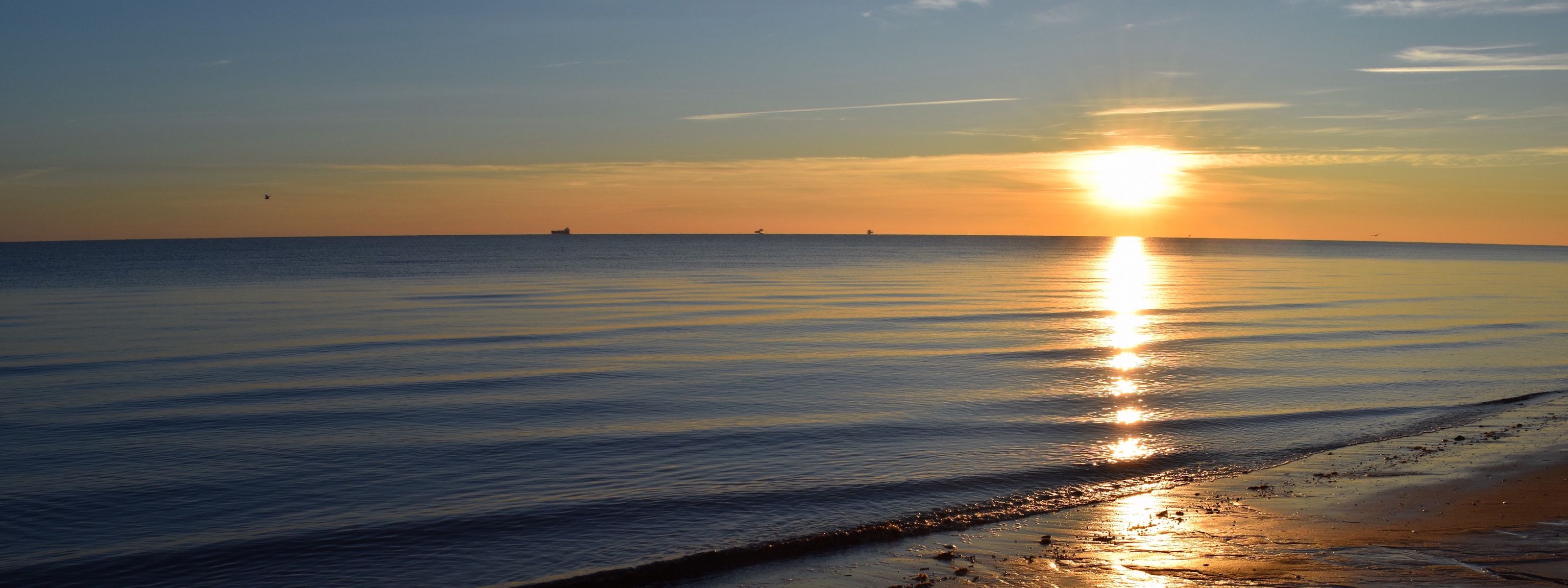 The sun sets over the wide expanse of Delaware Bay as the water gently laps the sandy shore.