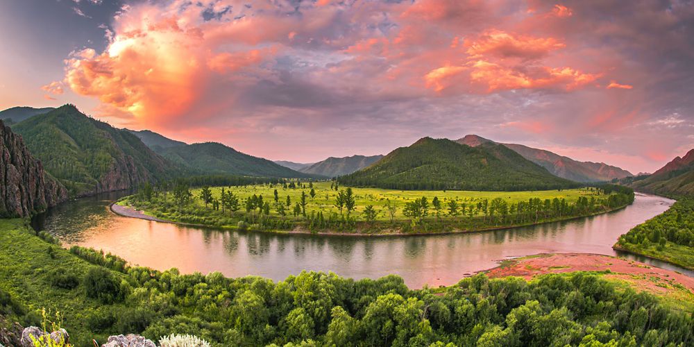 A panoramic view of a river reflecting a pink clouded sky.