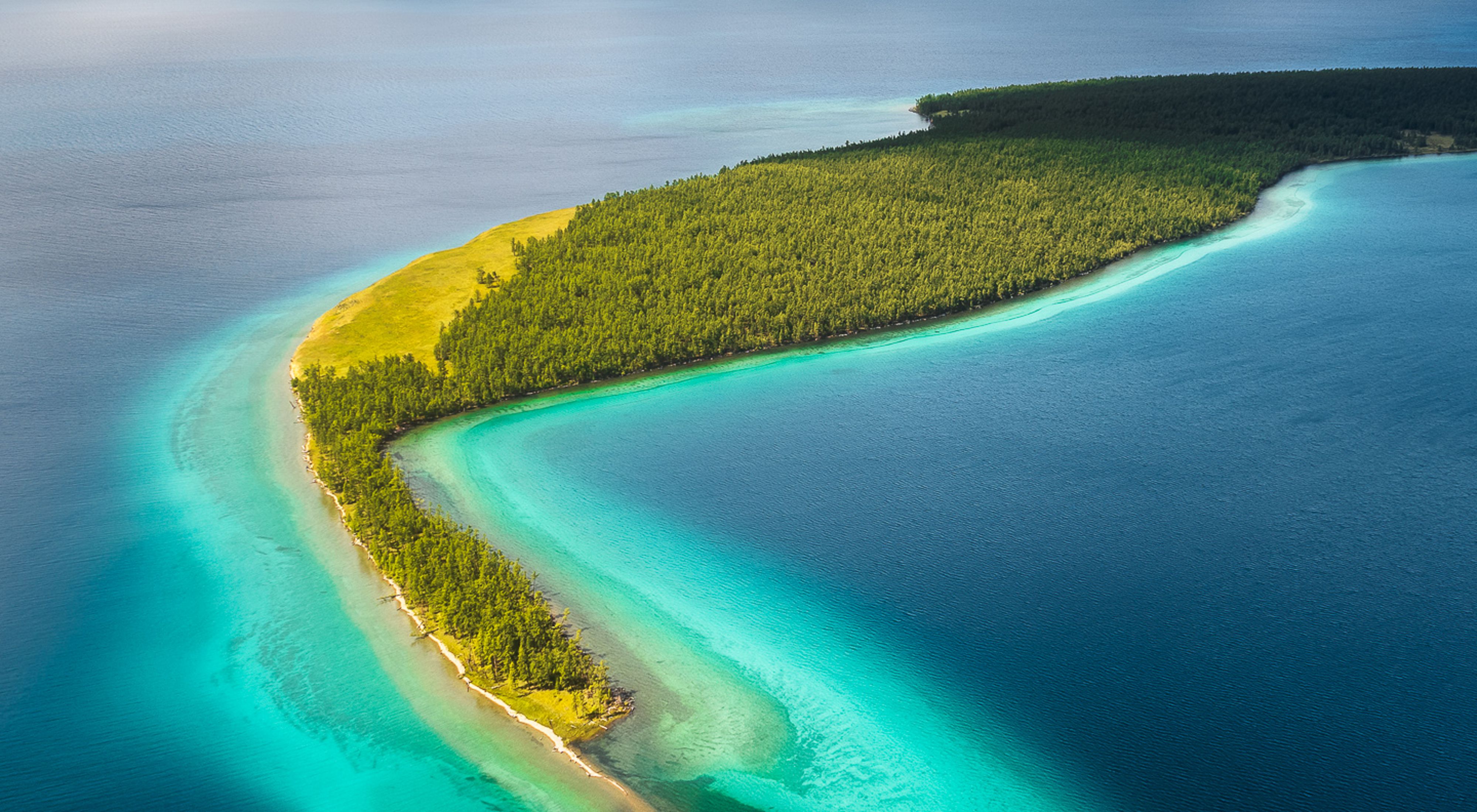 Aerial view of forested strip of land extending out into deep blue lake.