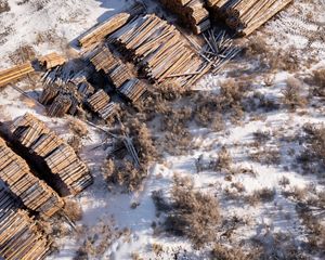 Aerial view looking down at piles and bundles of wood planks in a snowy landscape.