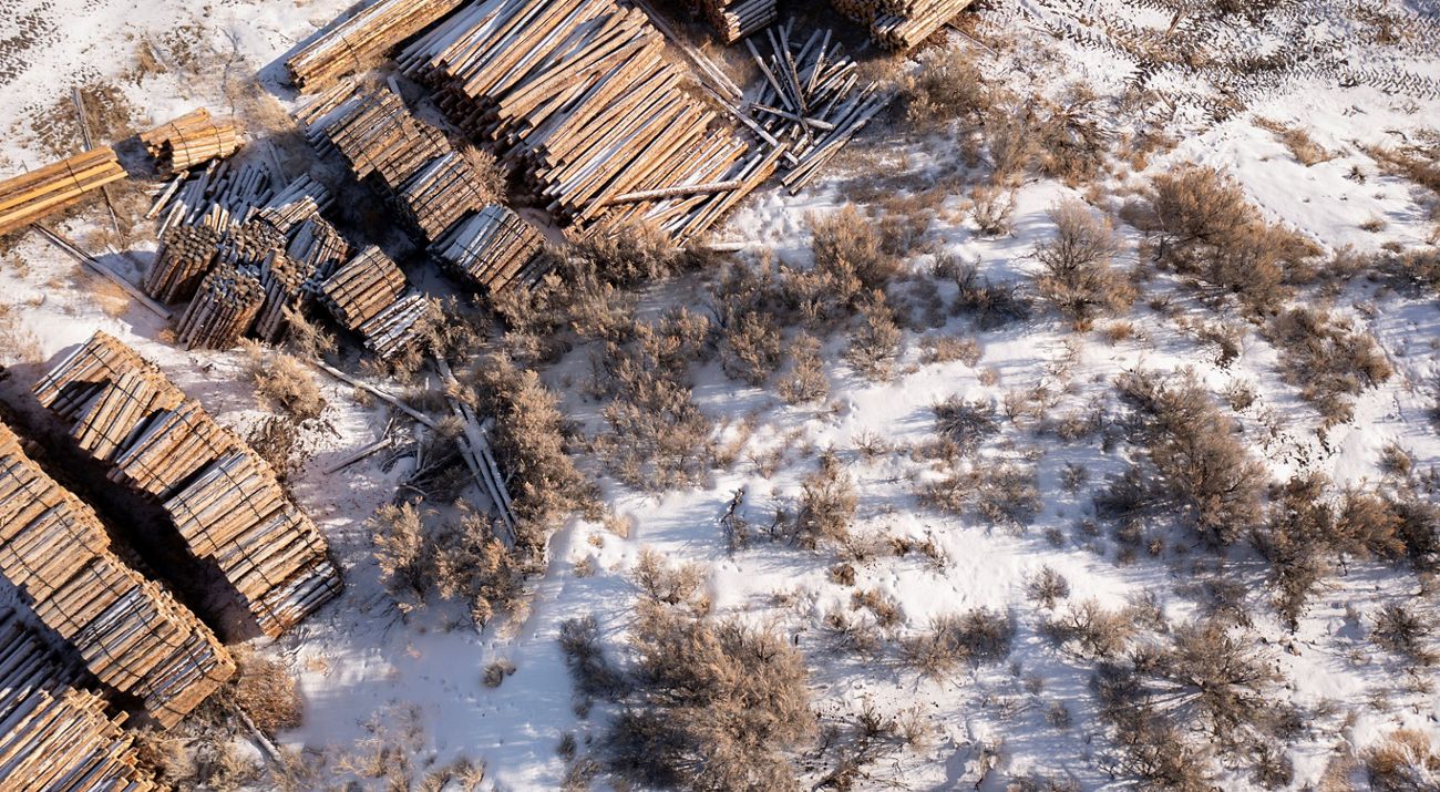 Aerial view looking down at piles and bundles of wood planks in a snowy landscape.