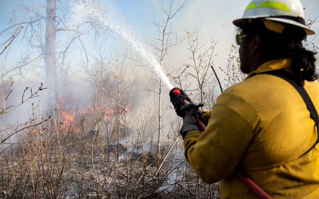 A fire technician spraying a hose onto flames.