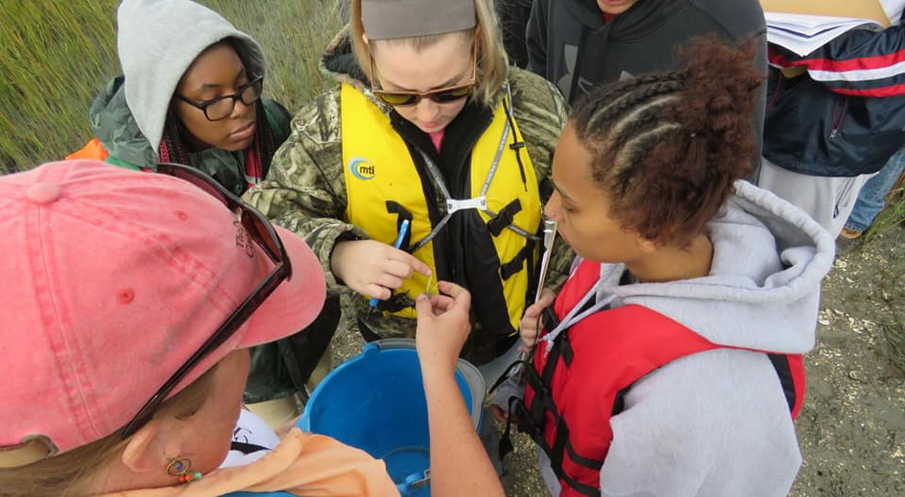 View looking down on four students crowding around a TNC staff member who is holding out a small fiddler crab for them to see.