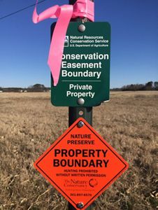 A rectangular sign reading, Conservation Easement Boundary Private Property, stands at the edge of an open field.