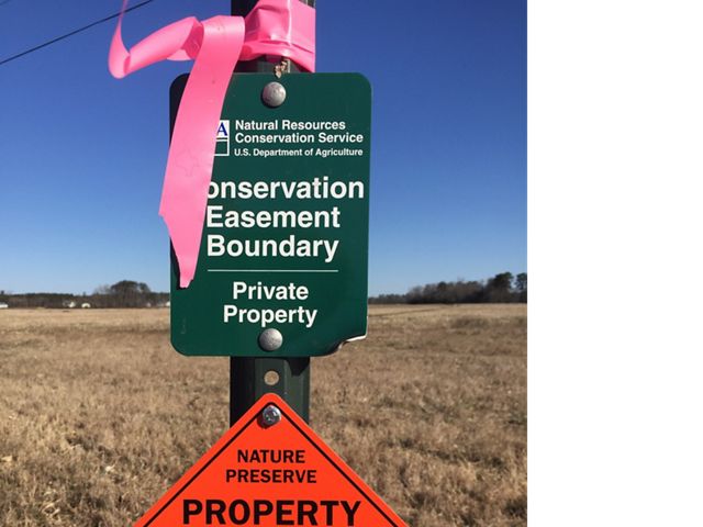 A rectangular sign reading, Conservation Easement Boundary Private Property, stands at the edge of an open field.