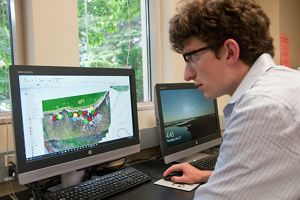 A young man sits at a desk and looks at a computer screen of a map.