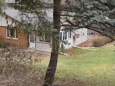A house sits behind a tree and a grass lawn.