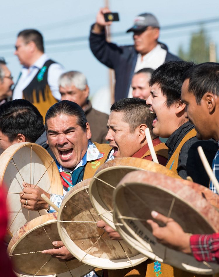 A group of eight men are yelling and beating drums