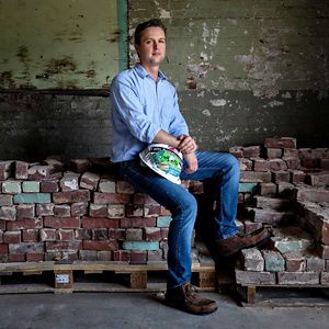 man holds a hardhat, sits on a pile of reclaimed bricks