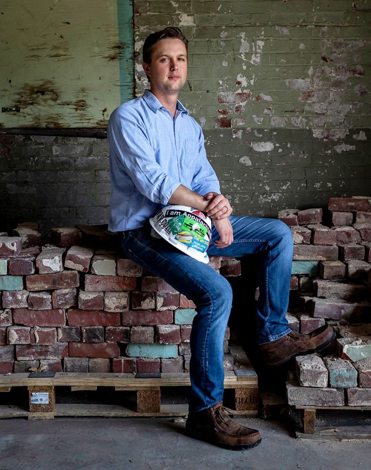 man holds a hardhat, sits on a pile of reclaimed bricks