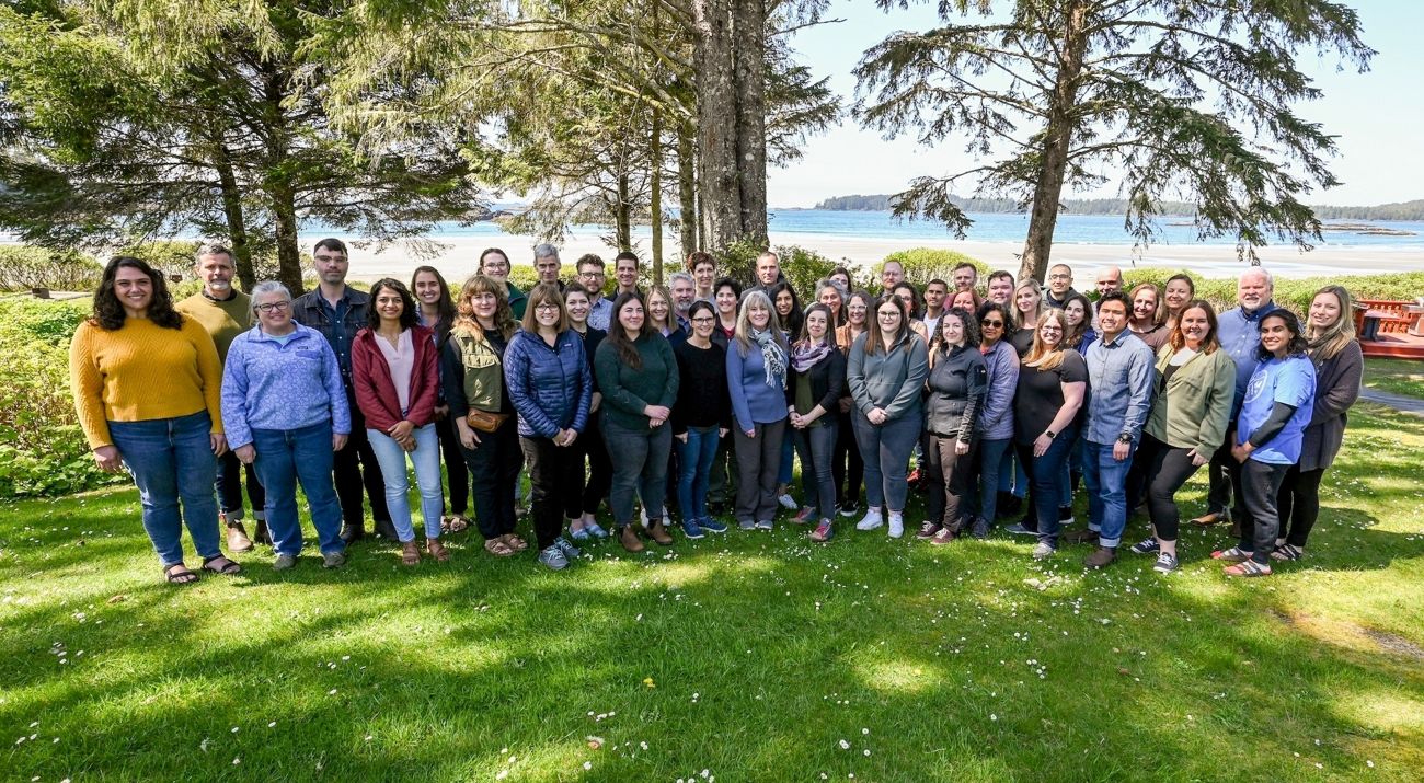 a group of about 30 diverse people posed in front of a scenic mountain view and smiling