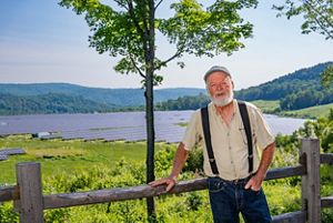 Man smiles at camera with a large solar array behind him in the background. 