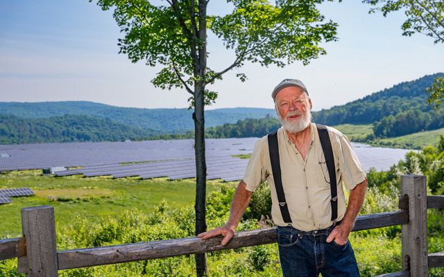 Man smiles at camera with a large solar array behind him in the background.