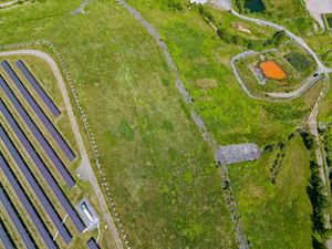 Aerial view of solar panels on the left and a pond on the right. 