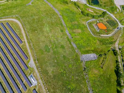 Aerial view of solar panels on the left and a pond on the right.