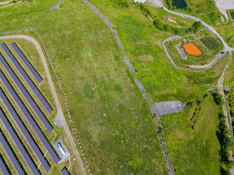 Aerial view of solar panels on the left and a pond on the right.