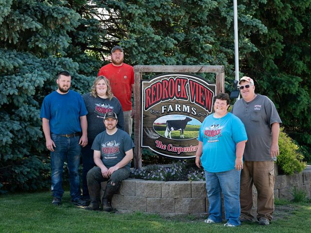 All six members of the Carpenter family stand and pose in front of the sign to their farm, which reads 'Redrock View Farms.'