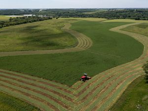 Aerial view of a red tractor cutting long, curving rows into a broad green field.