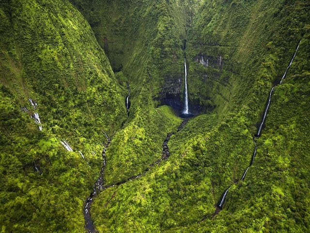 Aerial view of tall, thin waterfalls running down steep green cliffs at Wainiha Preserve in Kaua'i.