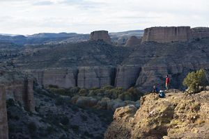 Three people take a break on a cliff with a canyon surrounding them during daylight.