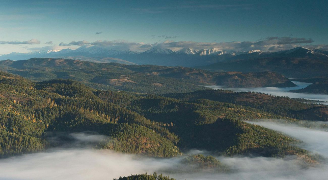 Aerial view of Blackfoot River cooridor with mountains covered in forest.