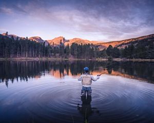 Photo of a man flyfishing in a pond in Rocky Mountain National Park, mountains in background.