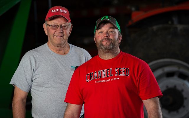 Portrait of Warren Luedke on the left and Travis Luedke on the right standing in front of farm equipment.