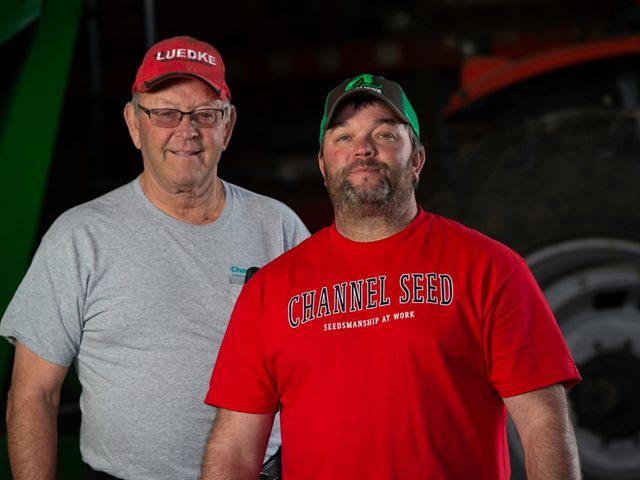 Portrait of Warren Luedke on the left and Travis Luedke on the right standing in front of farm equipment.