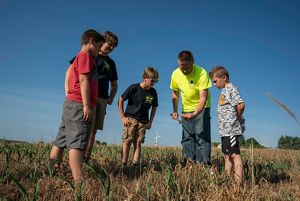 Nick Guilette stands in a field and holds a soil corer, which he shows to four young boys.