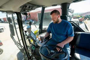 Carson Carpenter sits in the cab of a farm tractor and looks at gauges.