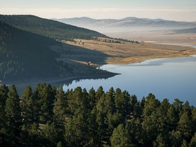 An aerial image of a large lake that meets mountains and a forest.