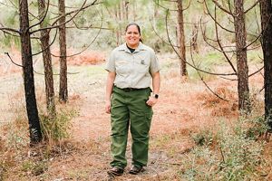 A woman stands in a clearing surrounded by small pine trees.