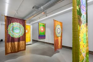 Colorfully painted saris suspended in an art gallery with white walls.