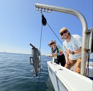 Two people on a boat reeling up a fish trap with a camera in it. 